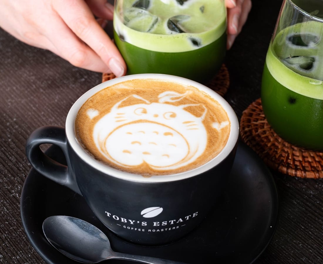 A cappuccino with cat latte art beside two iced matcha